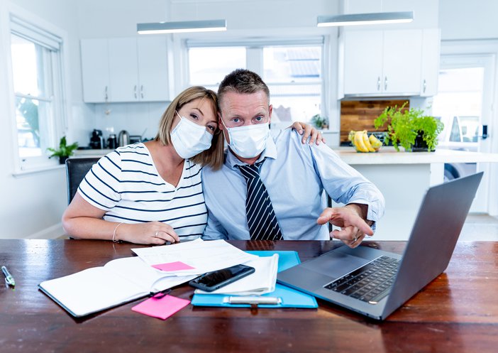 Masked couple at table with documents and computer.