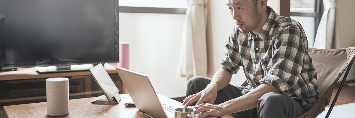 A person types on a laptop while sitting on the couch at home.