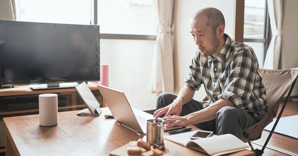 A person types on a laptop while sitting on the couch at home.