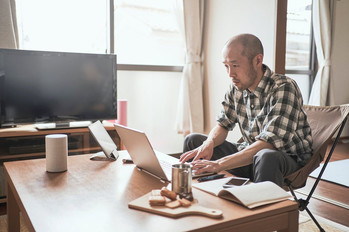 A person types on a laptop while sitting on the couch at home.