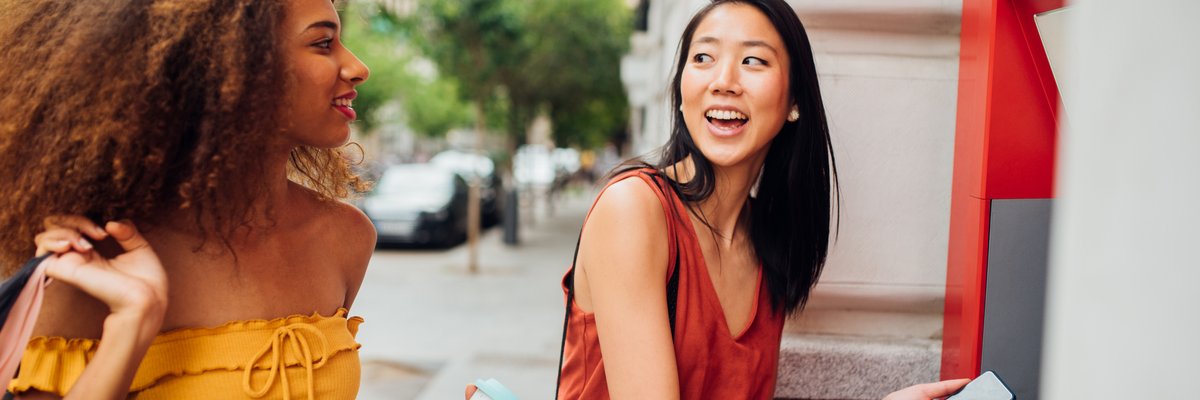 Two people holding shopping bags take money from an ATM machine while out on the town.