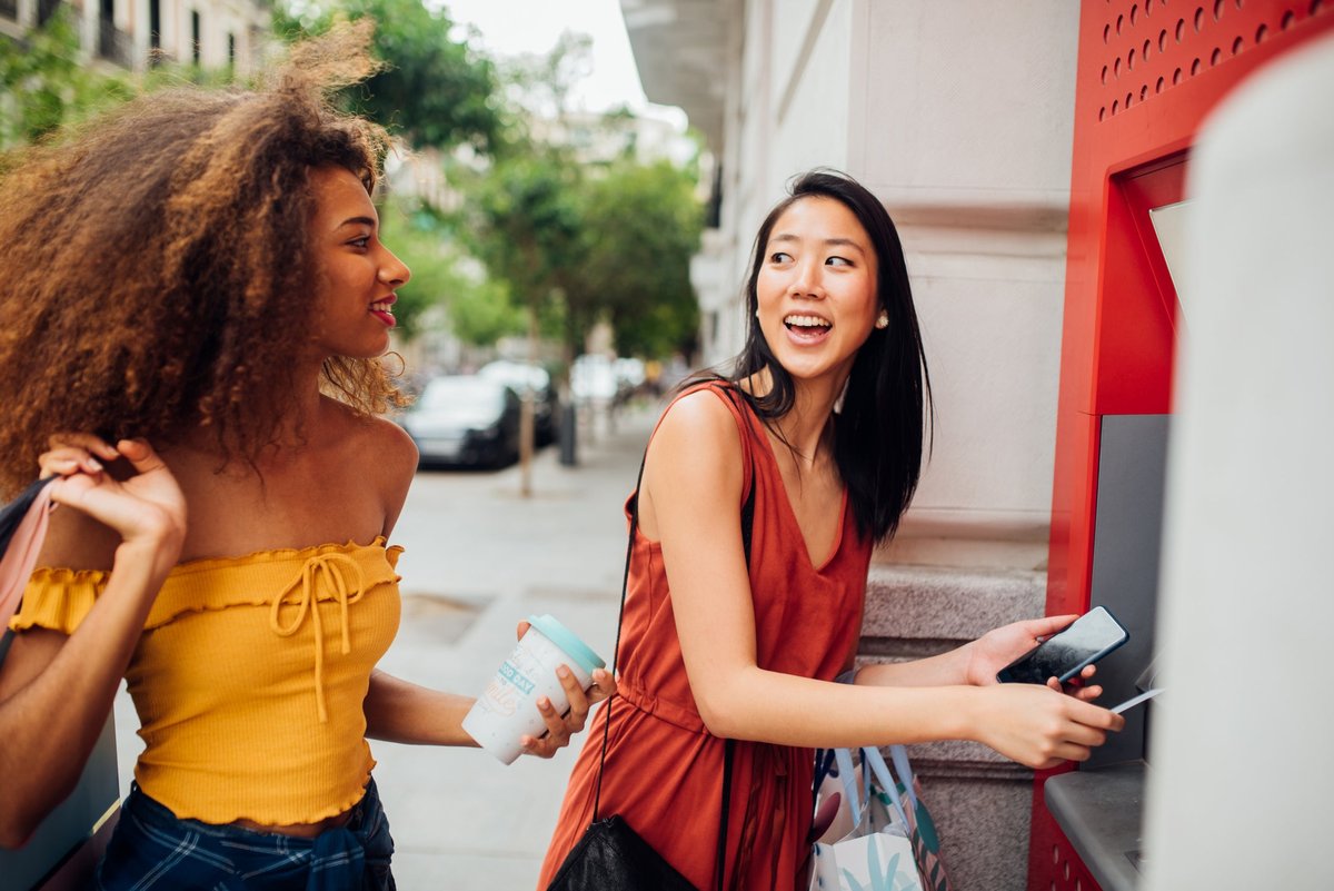 Two people holding shopping bags take money from an ATM machine while out on the town.