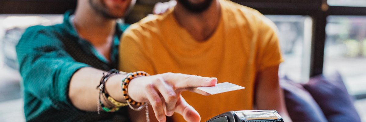 A couple smiles as they use a contactless credit card reader in a restaurant.