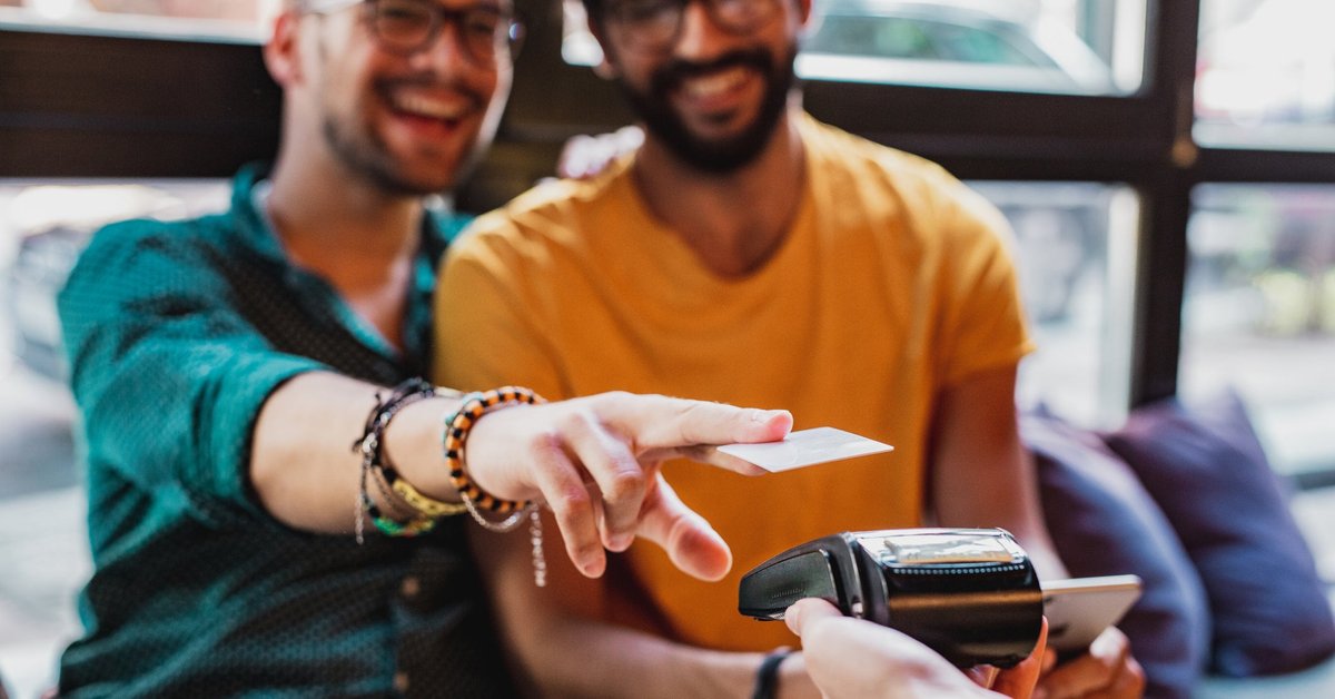 A couple smiles as they use a contactless credit card reader in a restaurant.