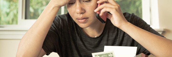 Stressed woman holding phone looks at bills.