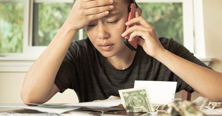 Stressed woman holding phone looks at bills.