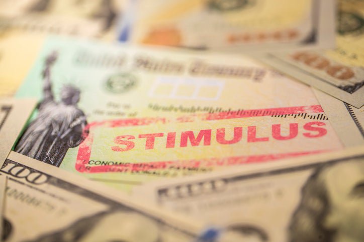 A photo of the economic stimulus check from the U.S. Treasury, with the word "STIMULUS" boldly stamped across it. The check is surrounded by $100 bills.