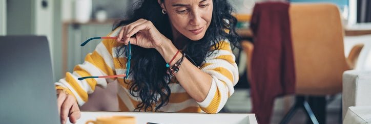 Woman holding glasses with one hand on computer keyboard.