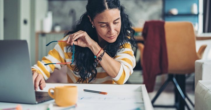 Woman holding glasses with one hand on computer keyboard.