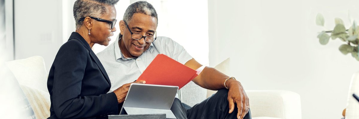 Two older adults discuss finances using a tablet on a couch.