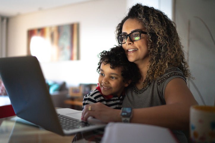 A parent and child smiling as they look at a laptop in their home.