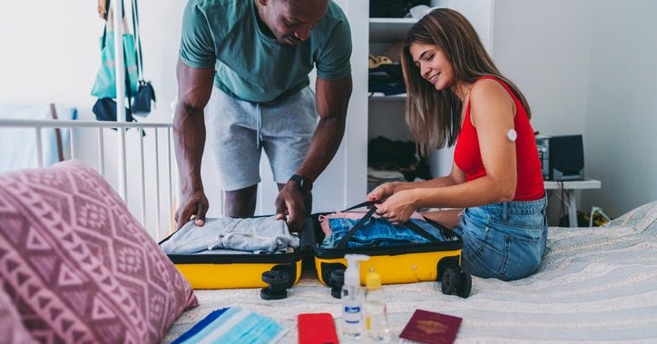 A couple packs a suitcase for traveling, including a wallet and passport.
