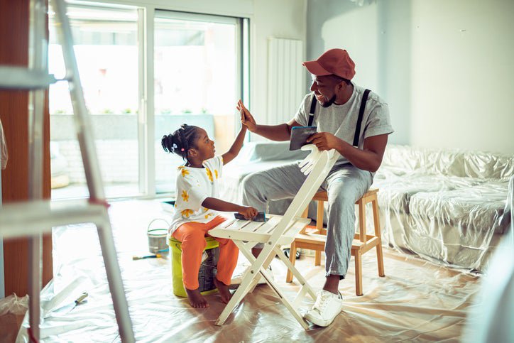 A father paints a chair with his daughter while remodeling their living room.