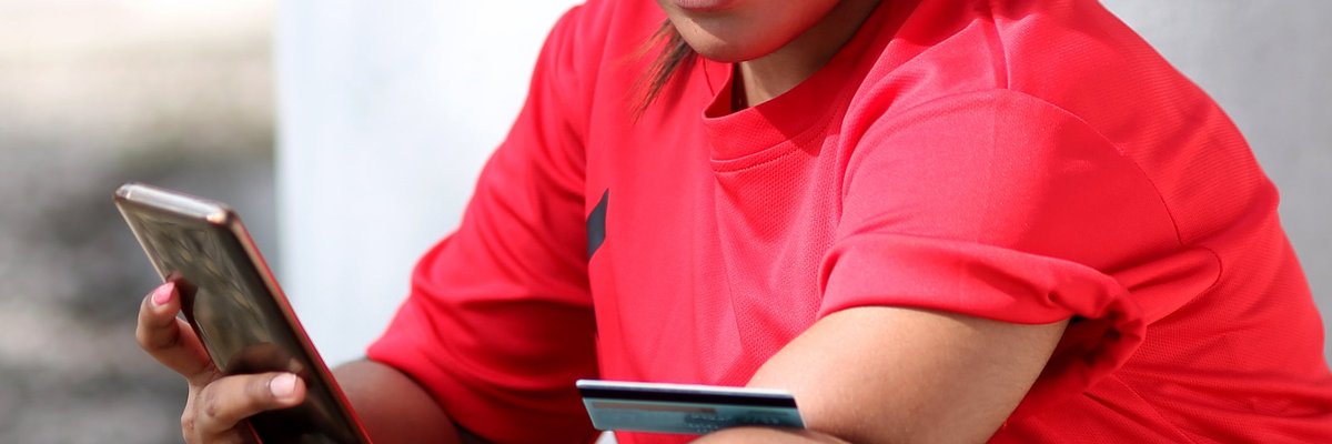 A person with an amputated left limb uses a credit card and smartphone to shop online while outside.