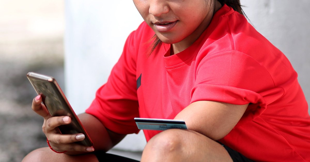 A person with an amputated left limb uses a credit card and smartphone to shop online while outside.