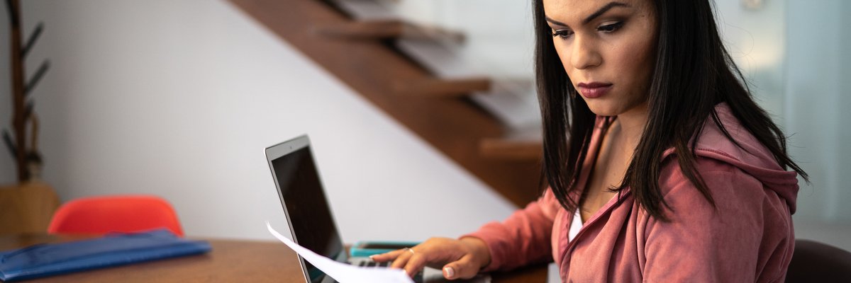 An adult sits at a desk at home looking through financial documents.