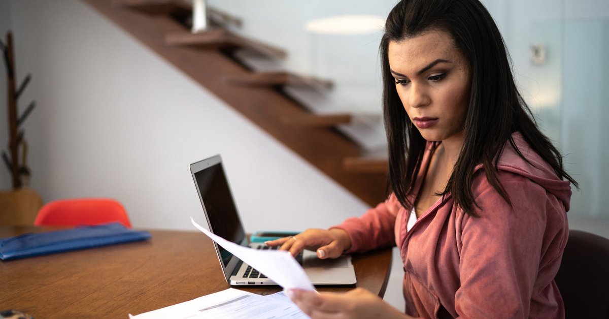 An adult sits at a desk at home looking through financial documents.