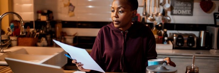 Young adult does their home finances at a laptop in the kitchen.