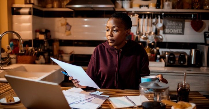 Young adult does their home finances at a laptop in the kitchen.