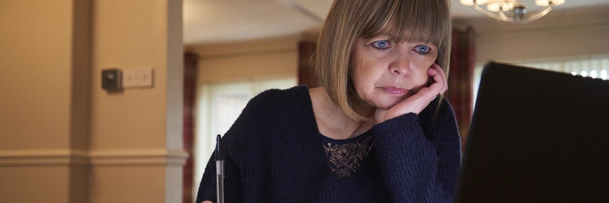 A middle-aged adult sorts their home finances with a laptop and notebook.