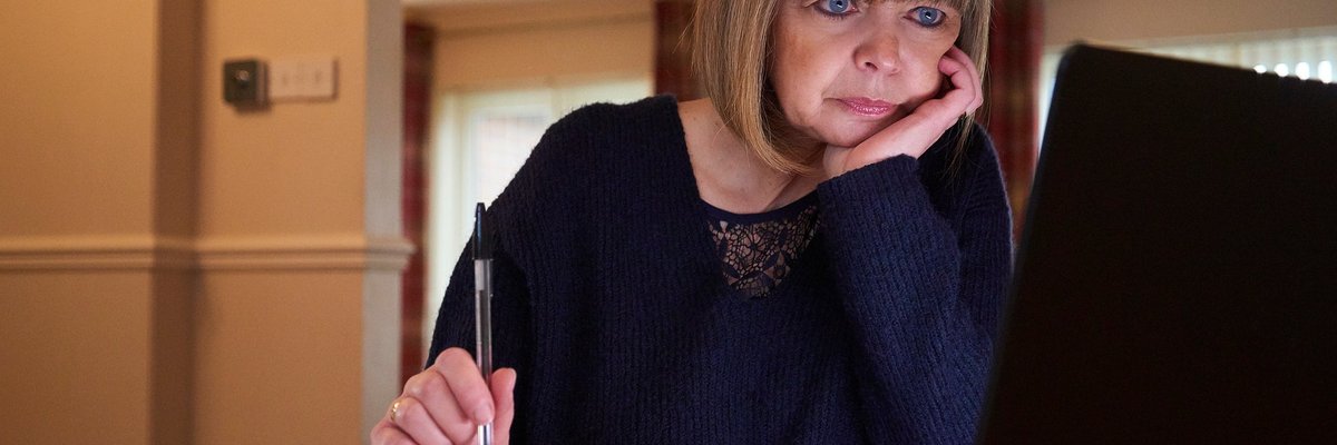 A middle-aged adult sorts their home finances with a laptop and notebook.
