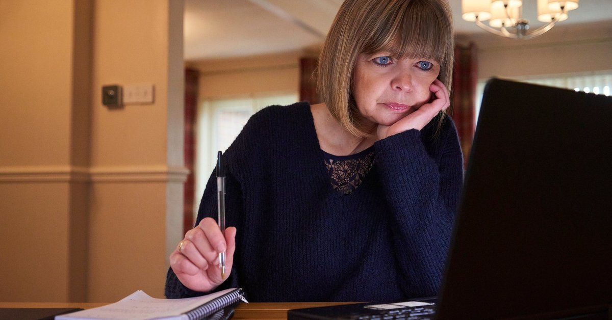 A middle-aged adult sorts their home finances with a laptop and notebook.
