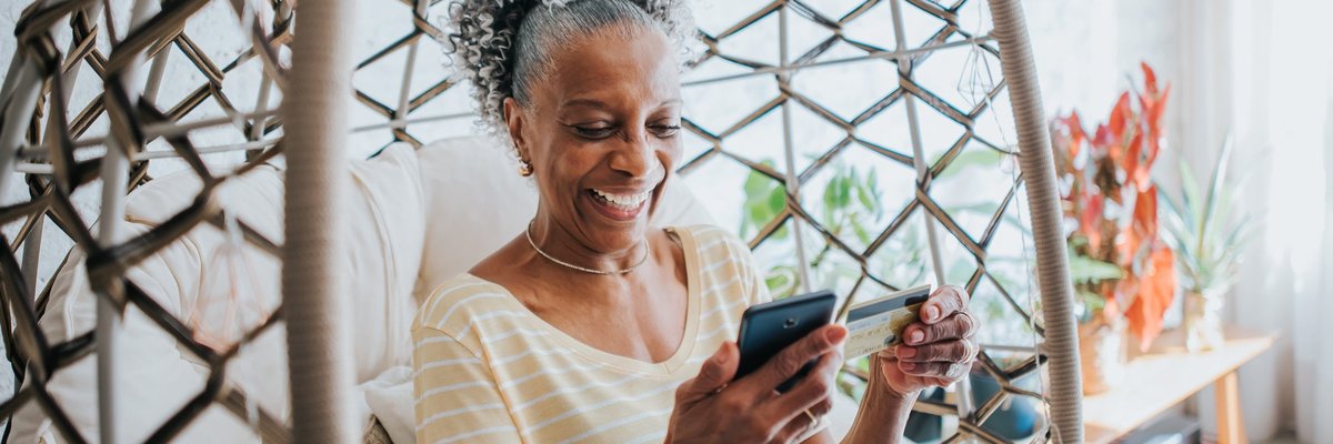 An older adult uses a credit card to make a payment on a smartphone in their living room.