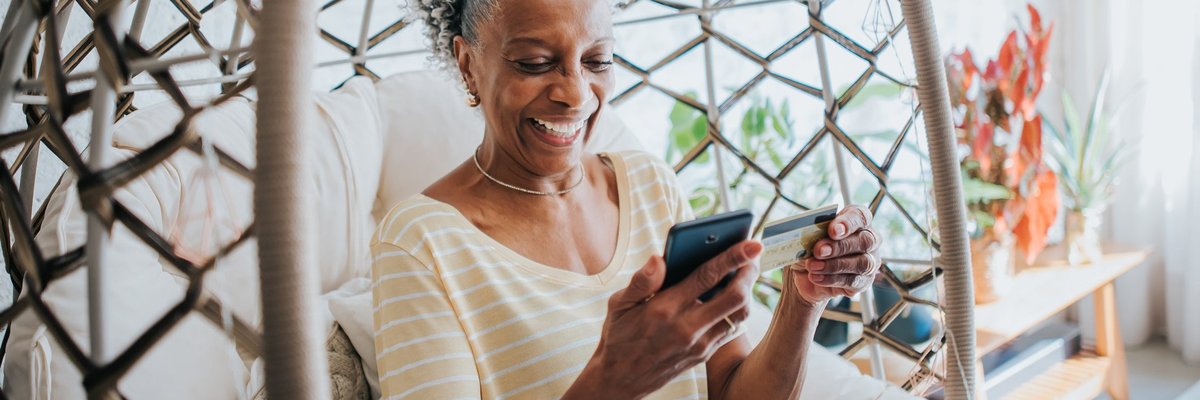 An older adult uses a credit card to make a payment on a smartphone in their living room.