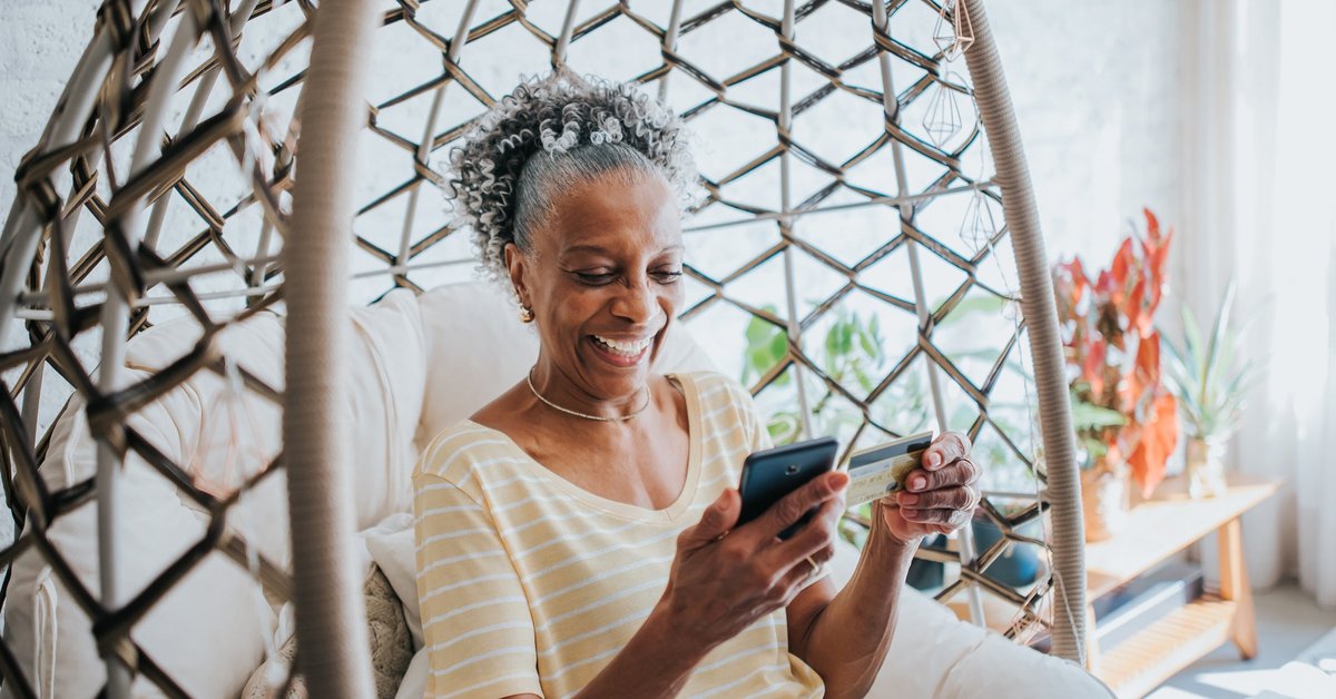 An older adult uses a credit card to make a payment on a smartphone in their living room.