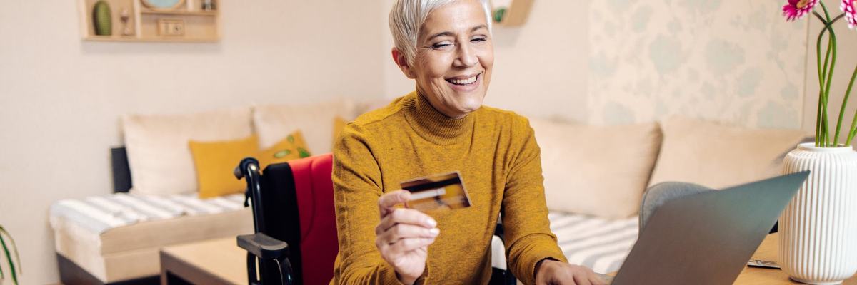 An older adult using a wheelchair buys things online with a credit card.