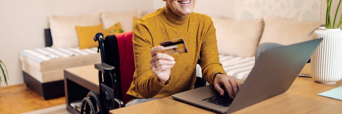 An older adult using a wheelchair buys things online with a credit card.