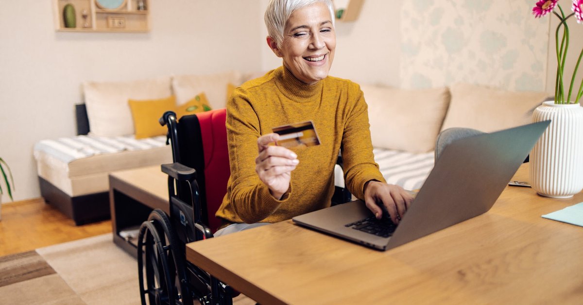An older adult using a wheelchair buys things online with a credit card.