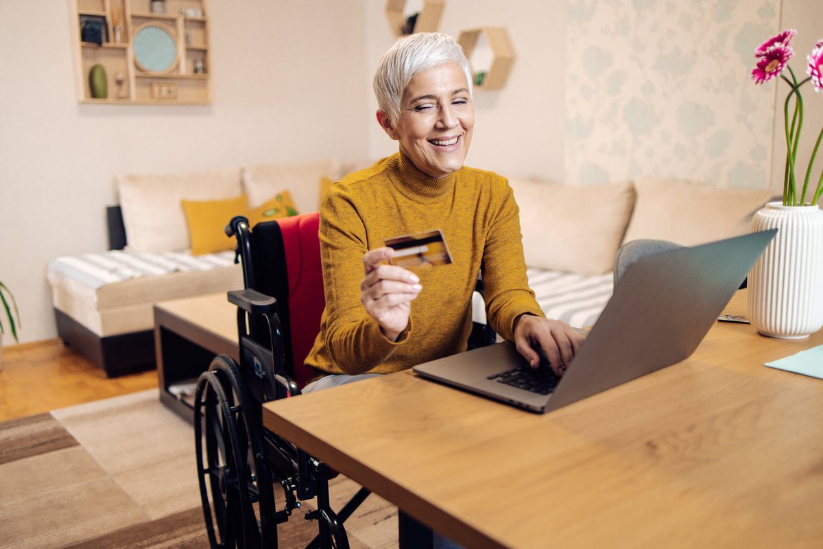 An older adult using a wheelchair buys things online with a credit card.