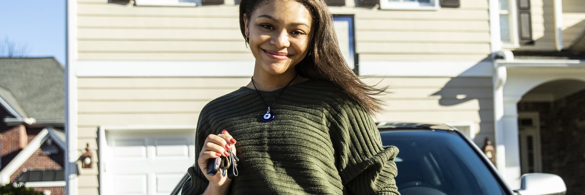 Young girl poses with keys in front of new car parked in front of a house.