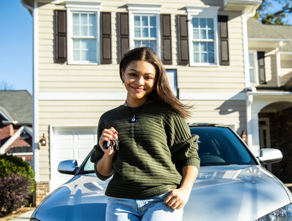 Young girl poses with keys in front of new car parked in front of a house.