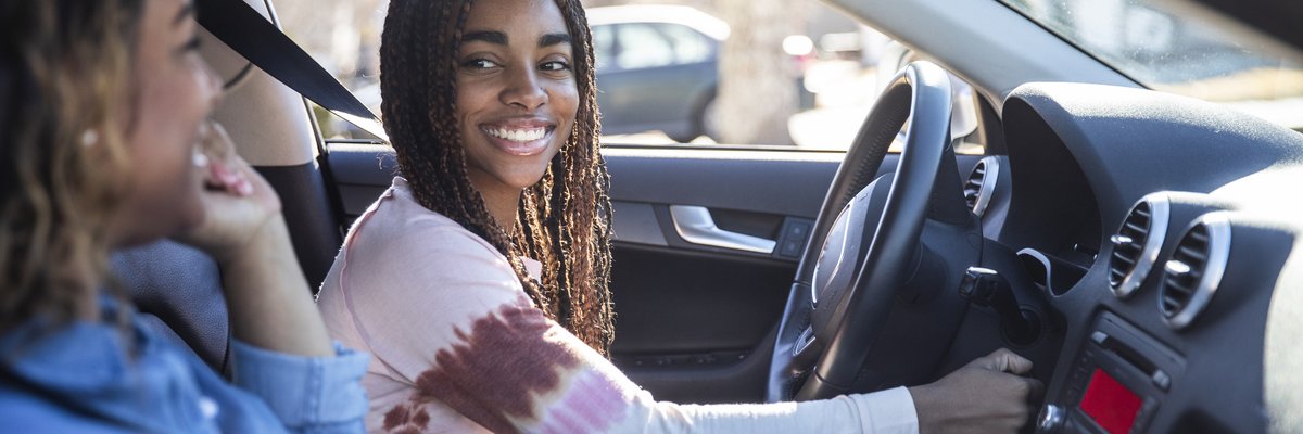 A teenager smiles at their mother as they turn on the car ignition.