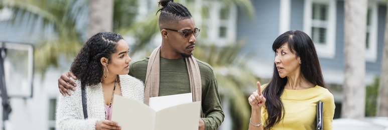 A real estate agent meeting in a parking lot with a young couple discussing mortgage documents.