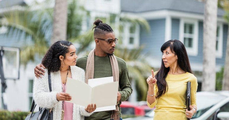 A real estate agent meeting in a parking lot with a young couple discussing mortgage documents.