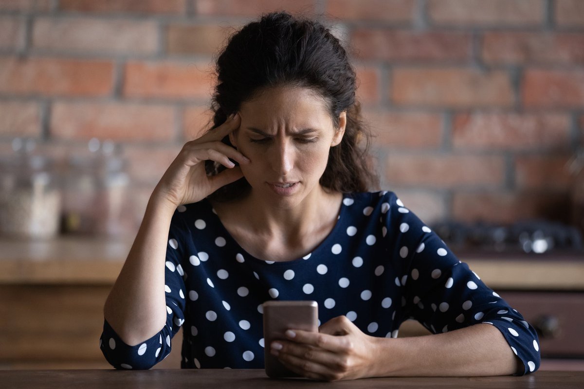 An upset person with a creased brow looks at their smartphone screen.