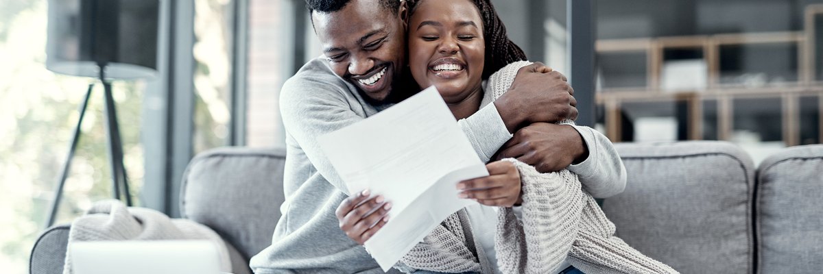 Happy couple embracing on the couch holding paperwork.