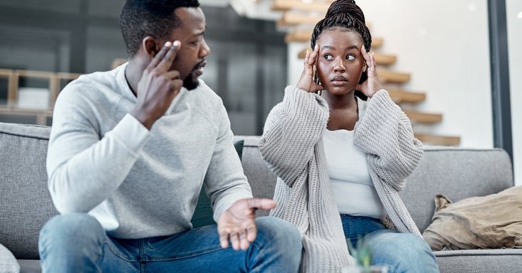 An African /American couple looks at each other worriedly. They sit in front of financial documents and a computer.