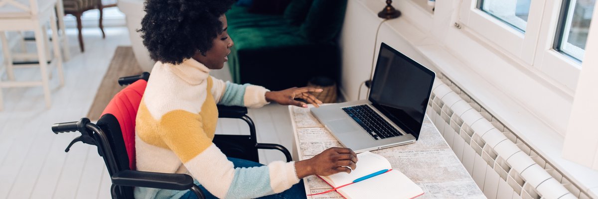A person using a wheelchair types on a laptop at a desk at home.