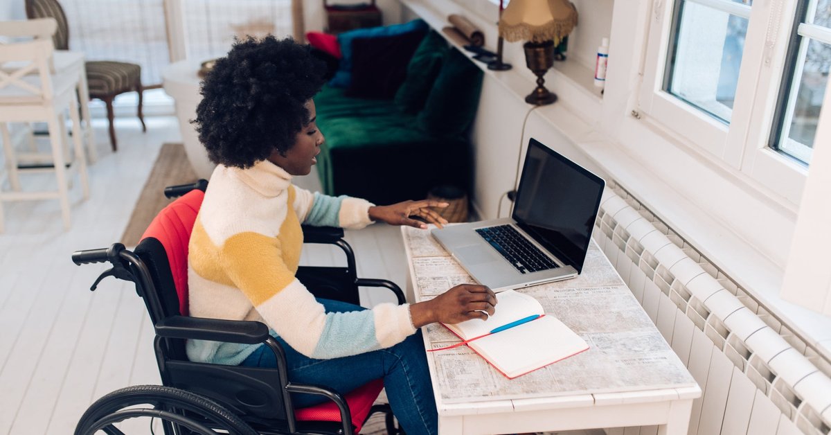 A person using a wheelchair types on a laptop at a desk at home.