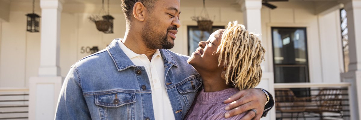 A couple embraces in front of their home.