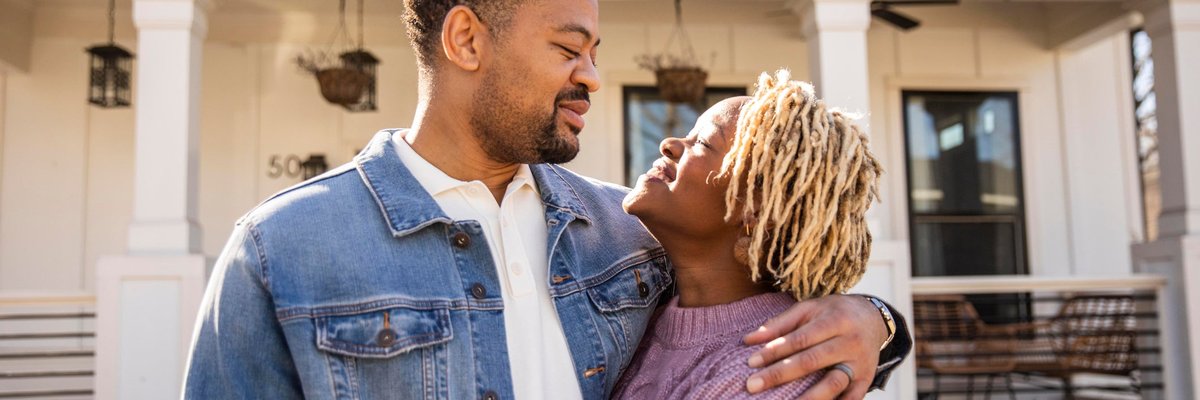 A couple embraces in front of their home.