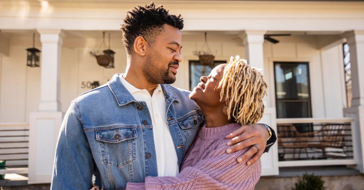 A couple embraces in front of their home.