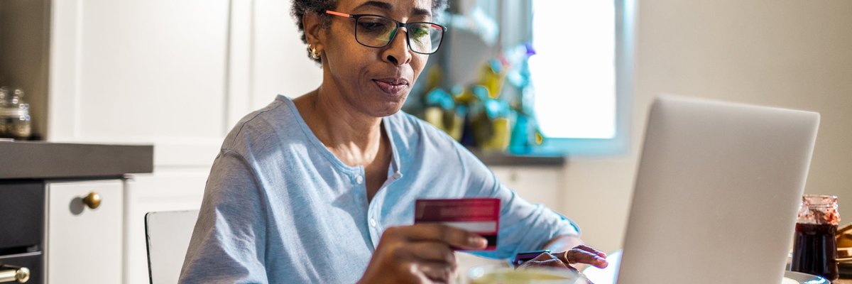 A person uses a credit card and laptop to purchase something online from their kitchen.