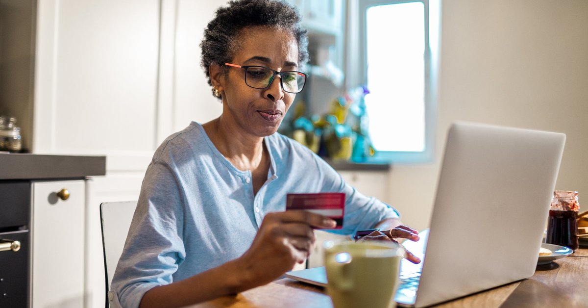 A person uses a credit card and laptop to purchase something online from their kitchen.