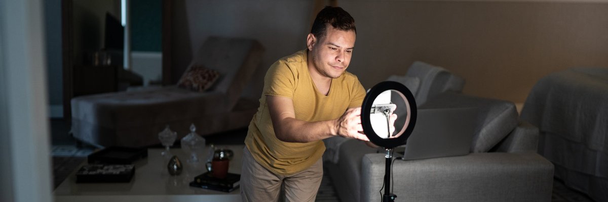 Someone sets up a ring light and camera in order to record video at home.