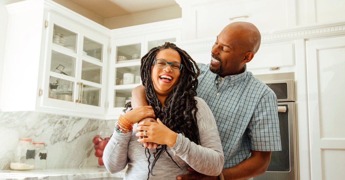 A middle-aged couple embraces happily in a kitchen.
